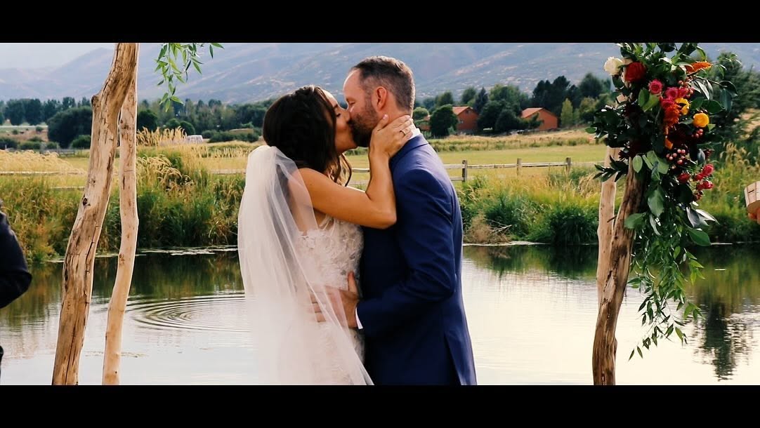 Newlyweds sharing a kiss during a lakeside ceremony